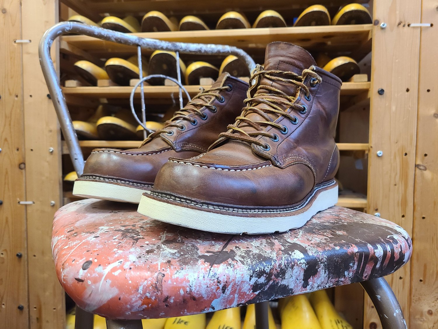 A pair of brown leather work boots on a paint-spattered stool in a shoe store.