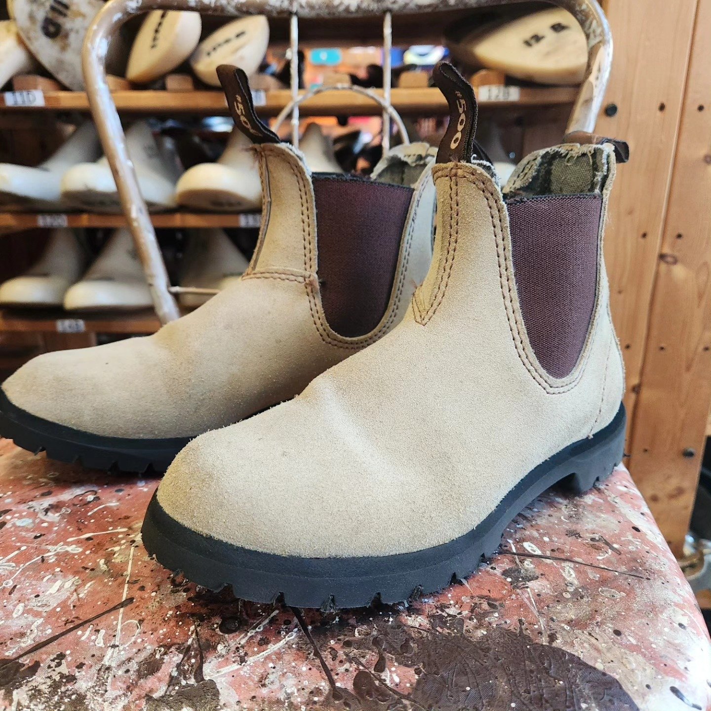 A pair of tan Blundstone boots with rebuilt black soles on the workshop bench